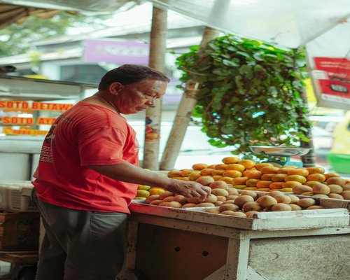 A friendly local vendor arranging fresh tropical fruits at an Indonesian traditional open air market stall